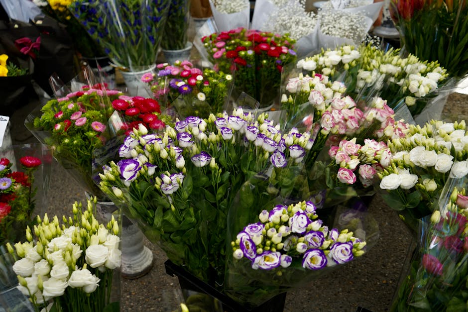 A vibrant display of fresh flower bouquets arranged on a table, featuring a variety of blooms including purple and white irises, pink and white roses, and small clusters of red, pink, and purple daisi