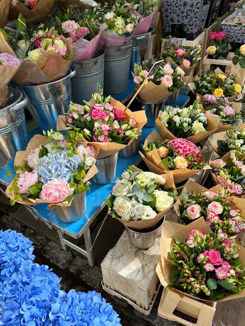A display of freshly arranged flower bouquets featuring pastel pinks, whites, blues, and soft greens, crafted with roses, hydrangeas, and lisianthus. The flowers are wrapped in brown kraft paper and p